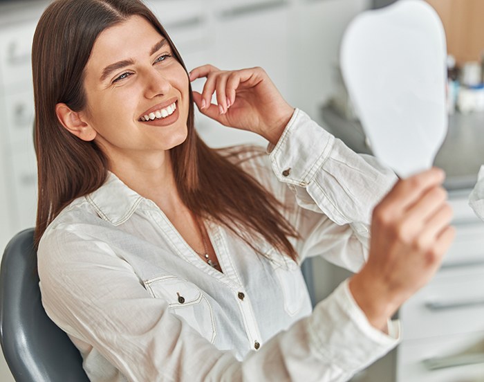Smiling woman in dental chair looking at handheld mirror
