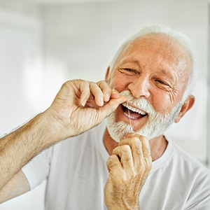 Man smiling while flossing in bathroom