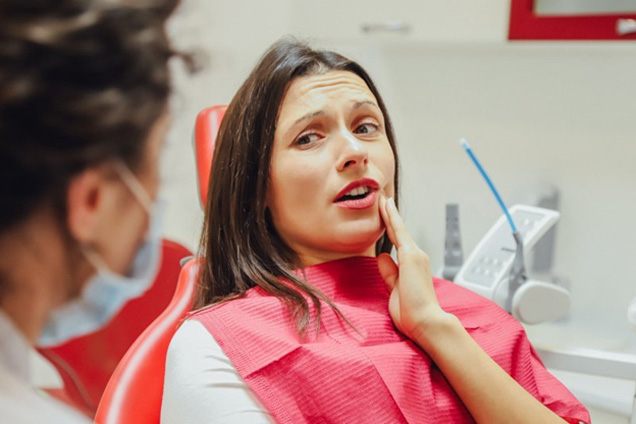 Woman rubbing her jaw and explaining symptoms to dentist
