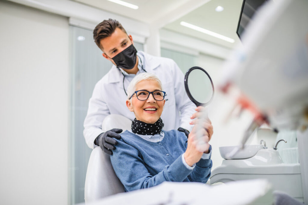 Beautiful senior woman having dental treatment at dentist's office. Dentist is wearing protective face mask due to coronavirus pandemic.