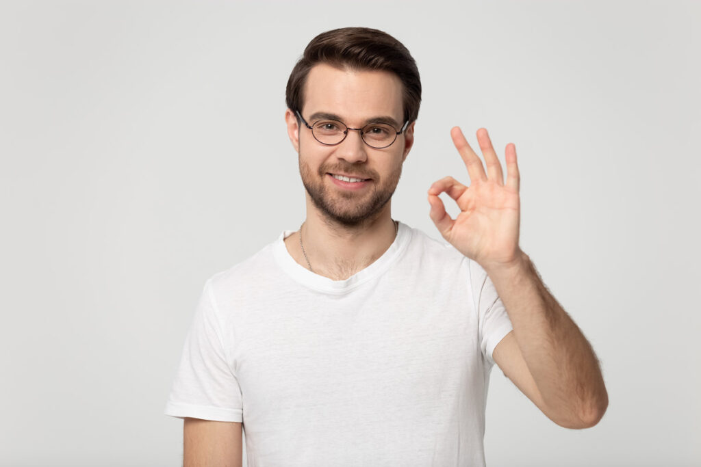 Head shot portrait young happy guy in eyewear showing okay gesture, isolated on grey white studio background. Millennial smiling male client agrees with promotional propose, accepting good offer.