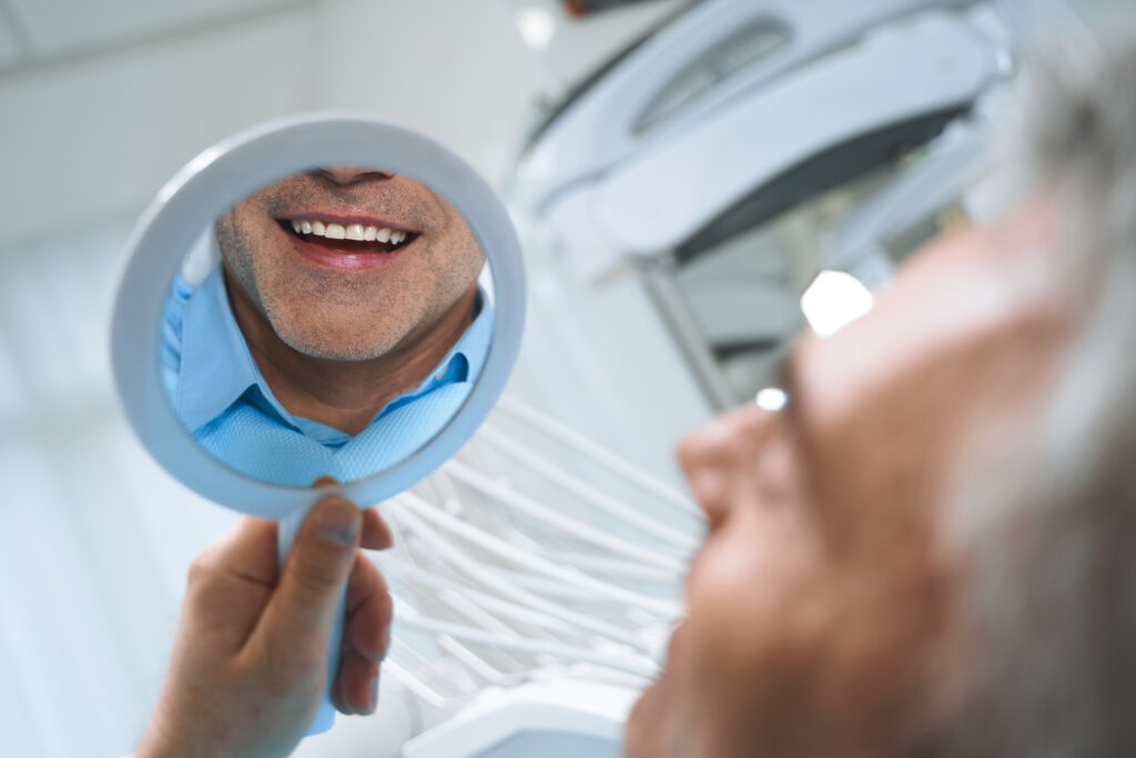 Jolly man is looking at mirror and enjoying reflectiong of his smile after dental procedures. Website banner