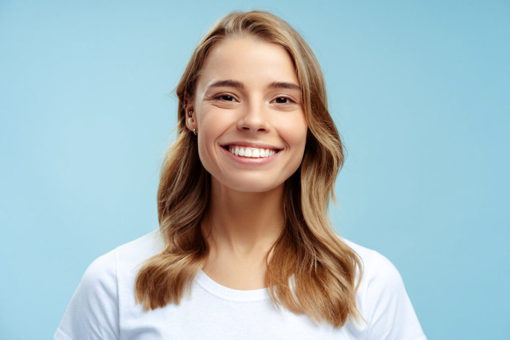Portrait of beautiful smiling woman with toothy smile looking at camera isolated on blue background, dental concept. Attractive gorgeous fashion model with silky wavy hair posing in studio