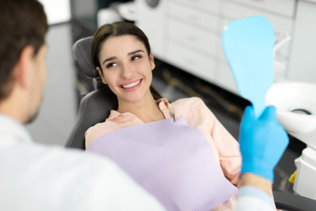 Female patient after dental treatment in clinic talking with doctor, woman sitting in chair in stomatological cabinet and enjoying her beautiful smile
