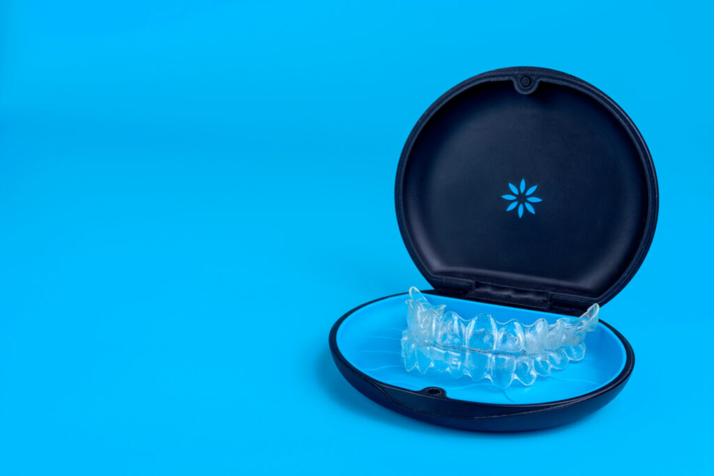 Black plastic case with transparent braces on blue background. Insivible removable retainers for orthodontic treatment.