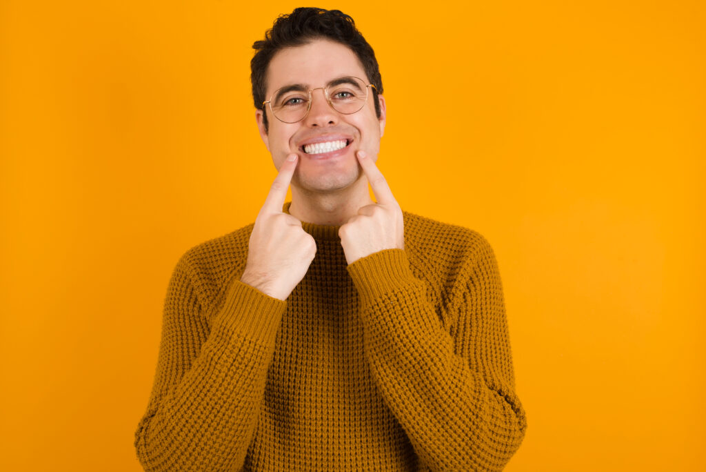 Strong healthy straight white teeth. Close up portrait of happy MDOEL with beaming smile pointing on perfect clear white teeth.
