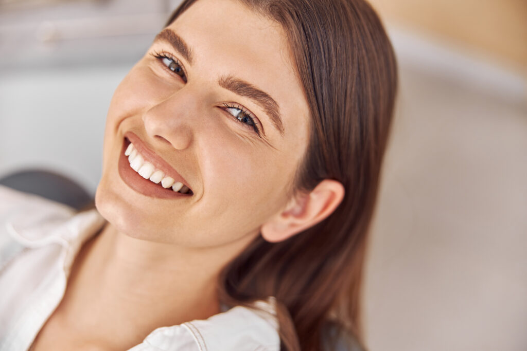 Attractive woman visiting dental clinic. Happy young woman sitting in dental chair at dentist office.
