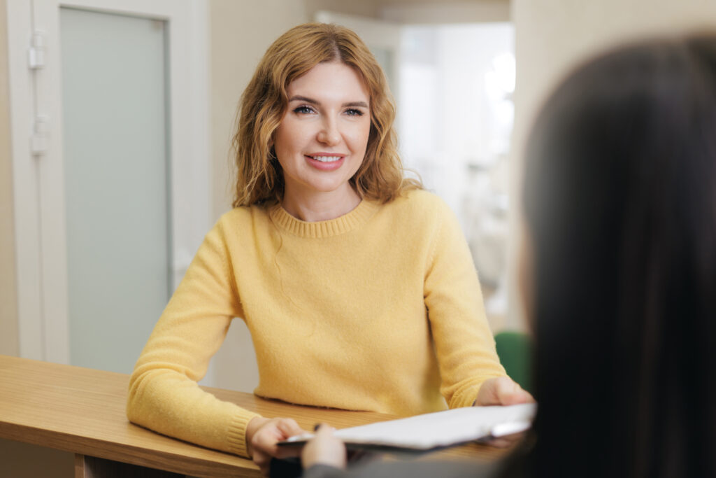 Client Caucasian female adult in yellow sweater interacting consultation at reception desk of clinic.