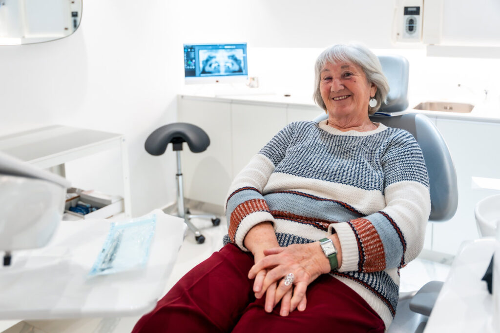 Elderly patient smiling and feeling comfortable during a dental checkup in a bright, modern clinic, highlighting senior oral care